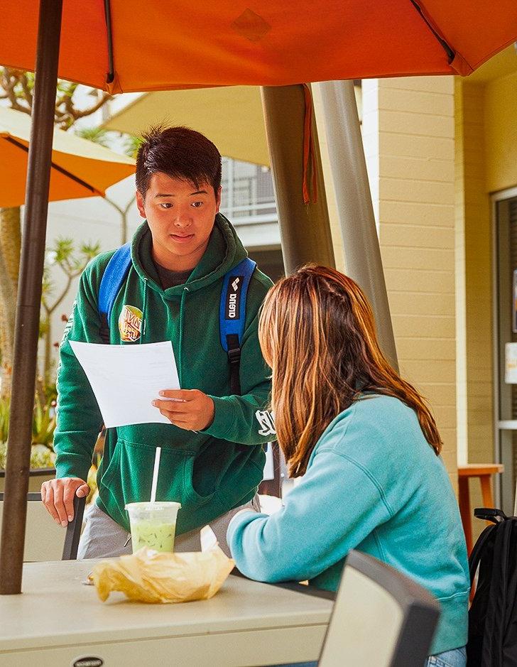 two students discuss a paper outside of Pit Stope Cafe